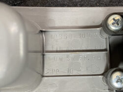 Close-up of a gray molded plastic panel with embossed alphanumeric codes, circular indentations, and two screws nearby on a dark surface.