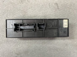 Black automotive control module (ECU) with two large connector housings and a small label on the end, resting on a gray concrete surface.