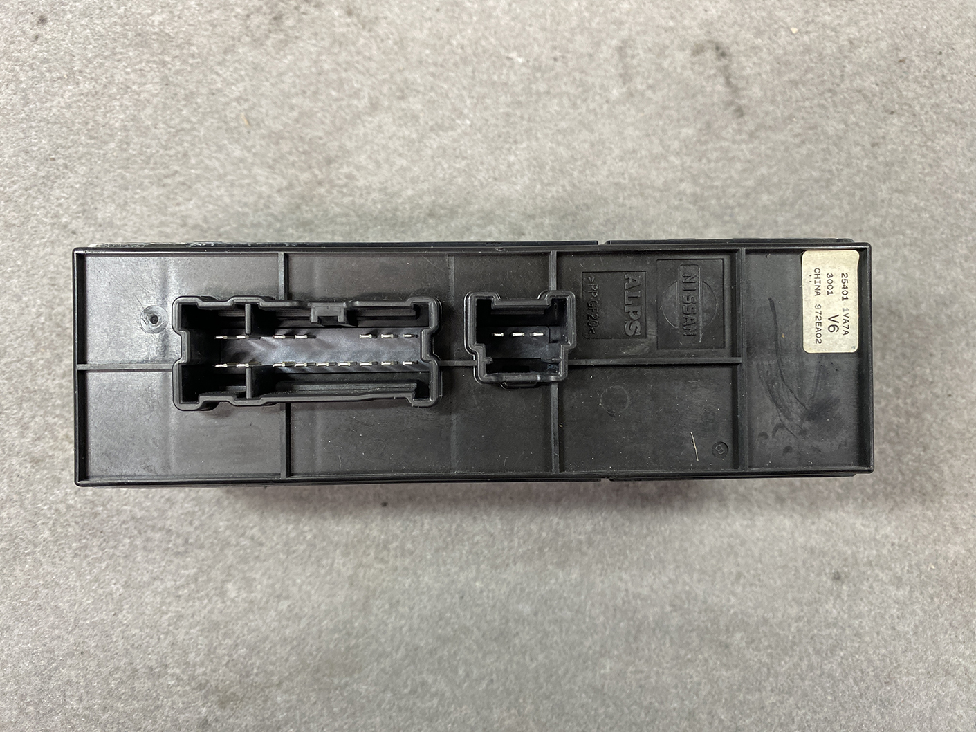 B488_6 NISSAN SERENA SUZUKI LANDY C26 Genuine Master Power Window Switch 25401 1VA7A » NZ.95 » JDM-PARTS NZ » JDM-PARTS NZ Black automotive control module (ECU) with two large connector housings and a small label on the end, resting on a gray concrete surface. NISSAN SERENA SUZUKI LANDY C26 Genuine Master Power Window Switch 25401 1VA7A » JDM-PARTS NZ