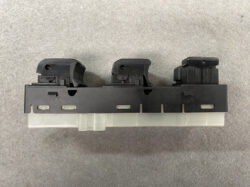 Close-up of a black plastic three-button rocker switch assembly on a dashboard panel, with a translucent base underneath (car window control module).