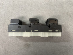 Three-button switch assembly mounted on a black rail with a clear/white connector at the bottom, likely an automotive or electronics control module