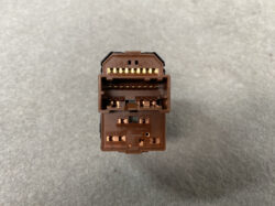 Close-up of a brown automotive multi-pin connector with gold-plated contacts, viewed head-on on a gray surface