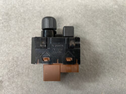 Close-up of a Nissan ABS module: black plastic body with a brown connector at the bottom and a large knob on top