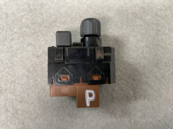 Close-up of a black LEGO brick assembly with a brown bottom piece bearing a white 'P' and a grey knob on top.