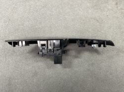 Black plastic automotive switch panel with multiple rocker switches and a mounting screw, viewed from the side (likely a car power window/lock control module).
