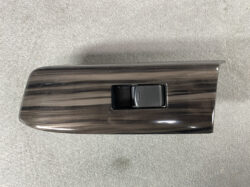Glossy dark woodgrain car door panel with a black power window switch in a recessed pocket.