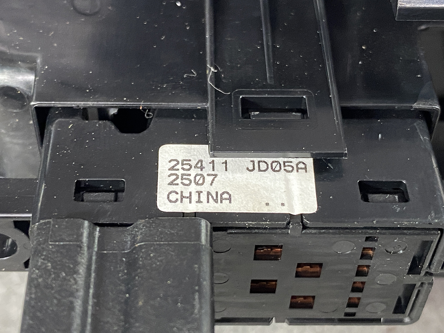 B491_4 NISSAN ELGRAND E52 Genuine Front Left Power Window Switch 25411 JD05A » NZ.95 » JDM-PARTS NZ » JDM-PARTS NZ Close-up of a black electrical breaker with a metal label reading '25411 JD05A 2507 CHINA' on top edge. NISSAN ELGRAND E52 Genuine Front Left Power Window Switch 25411 JD05A » JDM-PARTS NZ