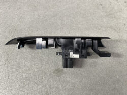 Black plastic automotive switch assembly with multiple mounting clips and a central electrical connector, likely a car door/window control module