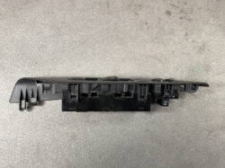 Automotive power window switch panel in black plastic, with multiple button housings, shown from the side on a gray surface.