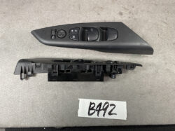 Driver-side car door control panel with power window switches, mirror adjust knob, and lock buttons on a black molded panel.