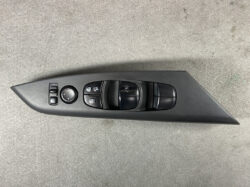 Car interior door panel with power window switches, mirror adjustment knob, and lock controls on a dark gray trim