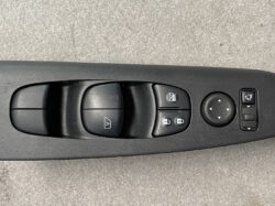 Car door control panel with power window switches, window lock, mirror adjust dial, and lock buttons on a black interior surface