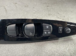 Car door control panel with power window switches, door lock buttons, and side mirror adjustment knob on a glossy black surface.