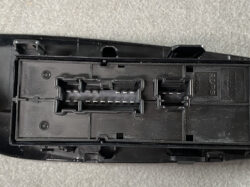 Black automotive electrical connector housing with two multi-pin receptacles and latch tabs, showing exposed metal pins inside.