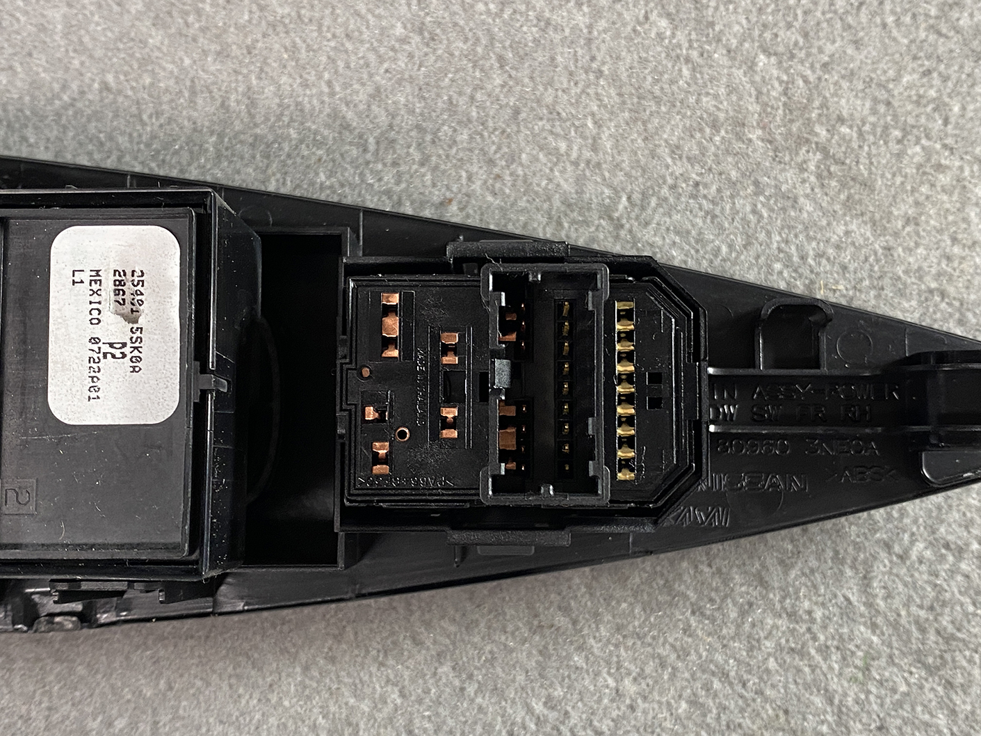 B494_7 NISSAN NOTE E11 Genuine Master Power Window Switch 25401 5SK0A » NZ.95 » JDM-PARTS NZ » JDM-PARTS NZ Close-up of a black automotive electrical connector with copper pins and a white label on the side. NISSAN NOTE E11 Genuine Master Power Window Switch 25401 5SK0A » JDM-PARTS NZ