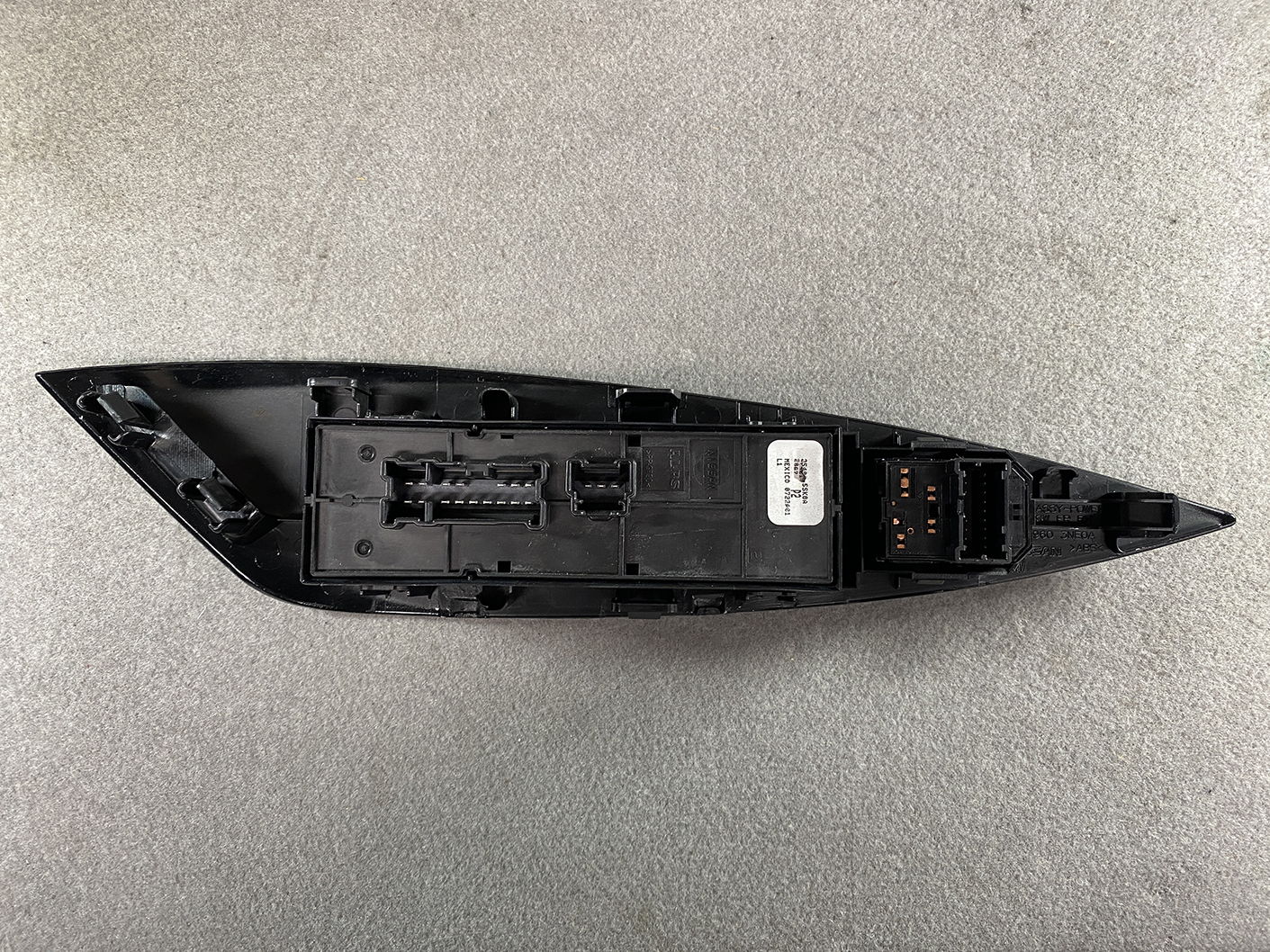 B494_8 NISSAN NOTE E11 Genuine Master Power Window Switch 25401 5SK0A » NZ.95 » JDM-PARTS NZ » JDM-PARTS NZ Dismantled black car side mirror housing showing wiring connector and mounting clips on a concrete surface NISSAN NOTE E11 Genuine Master Power Window Switch 25401 5SK0A » JDM-PARTS NZ