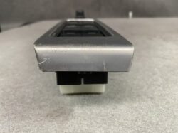 Close-up of a scratched silver metal rectangular panel mounted on a black plastic base on a gray surface.
