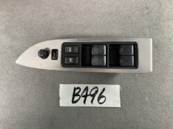 Car door interior panel with window control buttons and mirror adjuster on a brushed metal trim surface. The group includes four window switches, a central lock button, and a round mirror selector dial on the left.