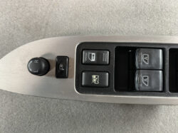 Driver-side car door panel with a circular mirror-adjustment knob (L/R), a window-lock switch, and four power window buttons on a silver armrest area.