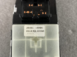 Close-up of a black electrical connector with copper contact pins above a silver housing, showing a white label with the text '25401 1AM0 0310 MA CHINA'.