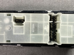 Close-up of a Nissan automotive electrical module with two plug-in connector housings on a translucent plastic enclosure.