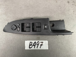 Driver-side car door control panel featuring window switches, lock button, and a circular mirror-adjustment pad on a black plastic panel.