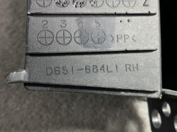 Close-up of a black plastic automotive part with molded part number D651-684L1 RH and PP recycling symbol on the surface, showing stamped circles with cross marks.