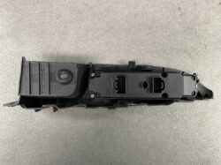 Black automotive electrical module with two rectangular multi-pin connectors and mounting screws, placed on a concrete floor.