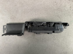 Disassembled black automotive control module with mounting bracket and exposed internal mechanism.