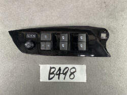 Black car door switch panel with window controls, mirrors, and lock buttons laid on a gray surface.