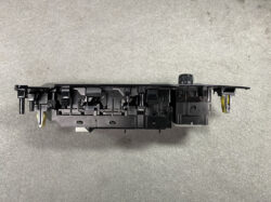 Black plastic automotive dash control module with multiple switch housings and a visible yellow wire harness, photographed on a gray surface.