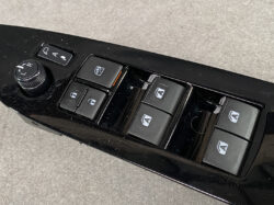 Car door control panel featuring four window switches, a window lock, and a side-mirror adjustment dial on the left; glossy black finish.