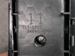 Close-up of a black plastic component showing raised '1 1' and stamped part numbers 757-0X5D 84040-47080, with a Phillips screw in a circular recess nearby.