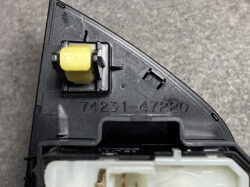 Close-up of a black automotive switch housing with a yellow rectangular component (relay/actuator) attached, labeled 74231-47220, on a gray surface