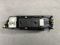Automotive switch assembly from a car door, featuring a white multi-pin connector on the left and yellow release tabs on the ends Readable and functional description of the component.