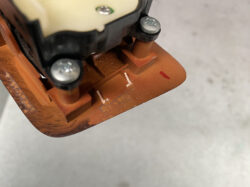 Close-up of an orange plastic switch base with two screws and a small brown post, showing wear on the housing.