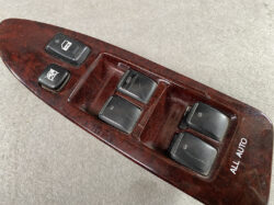 Car window control panel on wood-grain interior trim with four window switches and a lock button.