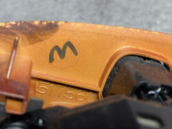 Close-up of orange molded plastic featuring a black stylized 'M' logo and the stamped number 51756; part of a device or tool interior.