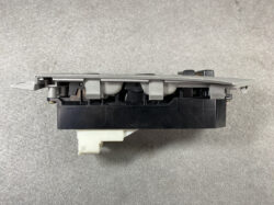 Side view of a gray and black automotive radio/module with a white connector at the bottom and mounting clips