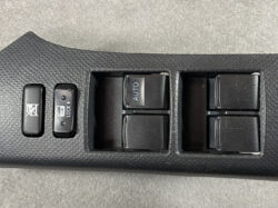 Black textured car door panel showing power window switches (one labeled AUTO) and left-side window/child lock buttons.