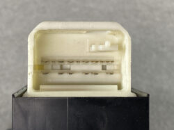 Close-up of a white rectangular multi-pin electrical connector with exposed metal terminals atop a dark surface.