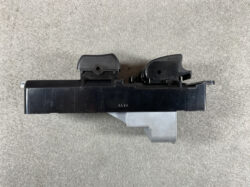 Black automotive electrical module with two top latch housings and a gray connector below on a gray surface.