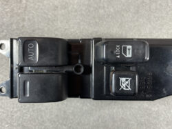 Close-up of a car window control panel: left switch labeled AUTO, right-side switchs for lock and window lock/dotch icons on a dark door panel