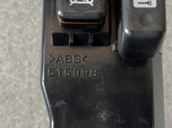 Close-up of a black plastic component stamped with 'ABS' and the number 515098, with a small switch/lever and a recessed slot visible in the scene.