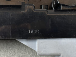 Close-up of a black plastic device housing with the molded code '1A18' and a silver metal surface below.