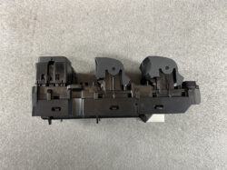 Black plastic automotive switch/module with two curved actuator housings and mounting clips on a gray surface