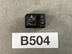 Car side-mirror adjustment switch (L/R with arrows) next to a vertical A control, on a gray surface with label B504