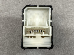 Front-facing view of a white plastic electrical connector inside a black housing, showing a row of copper contact pins.