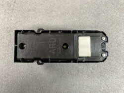 Toyota automotive door actuator module, black plastic housing with a white rectangular actuator block at one end and two screws visible on the side