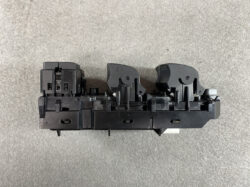Black plastic electronic switch assembly with two curved lever actuators on a gray surface, likely an automotive control module.